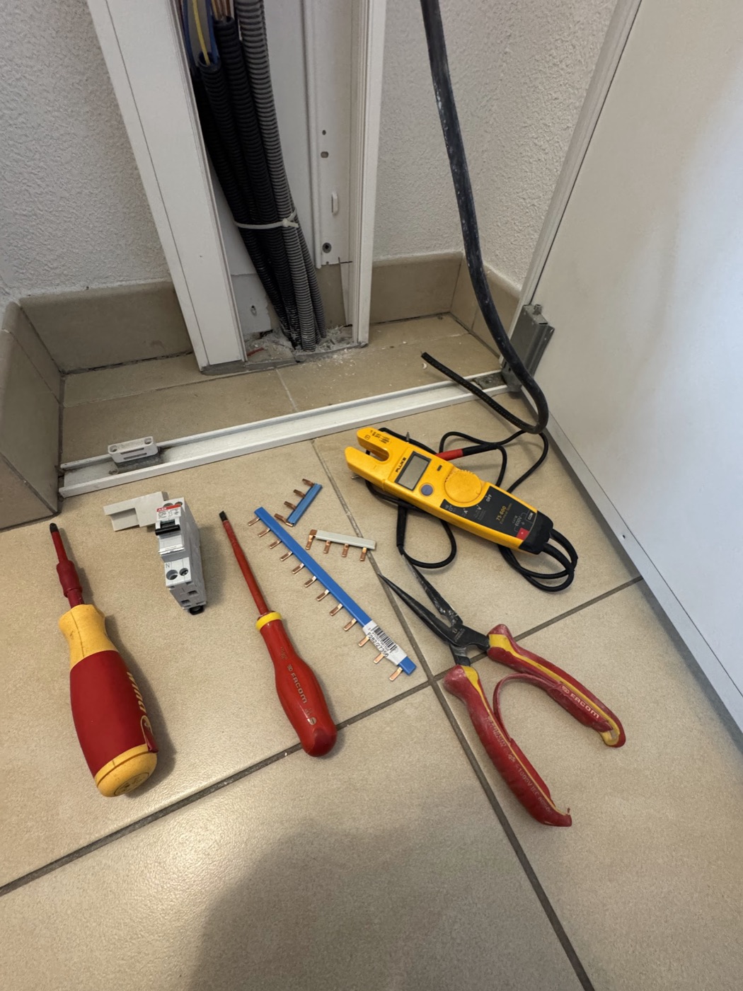 Outillage professionnel d'électricien : tournevis isolés, testeur Fluke, disjoncteur et peignes de répartition